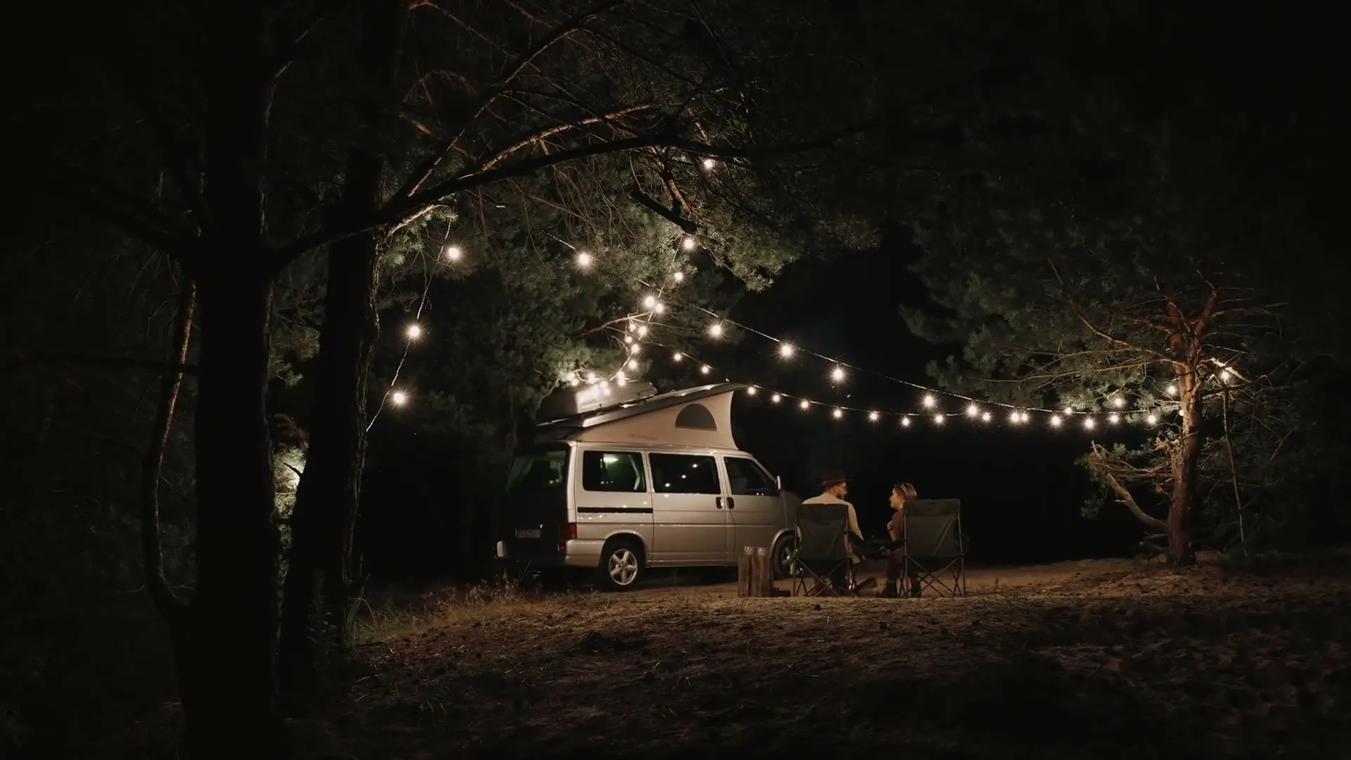 Camper mit Aufstelldach unter Lichterketten am Abend